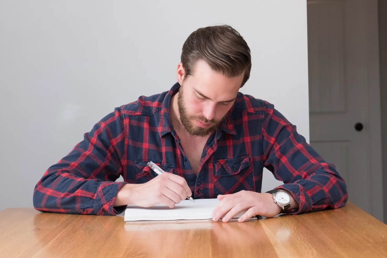 Patrick Dohan drawing at a solid oak table, pen in hand over a sheet of paper.